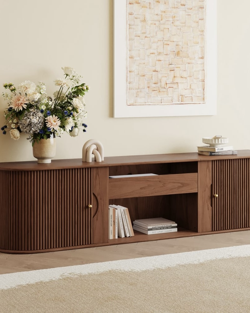 Buffet en bois avec portes et tiroirs texturés coulissantes, vase blanc, livre et art mural minimaliste.