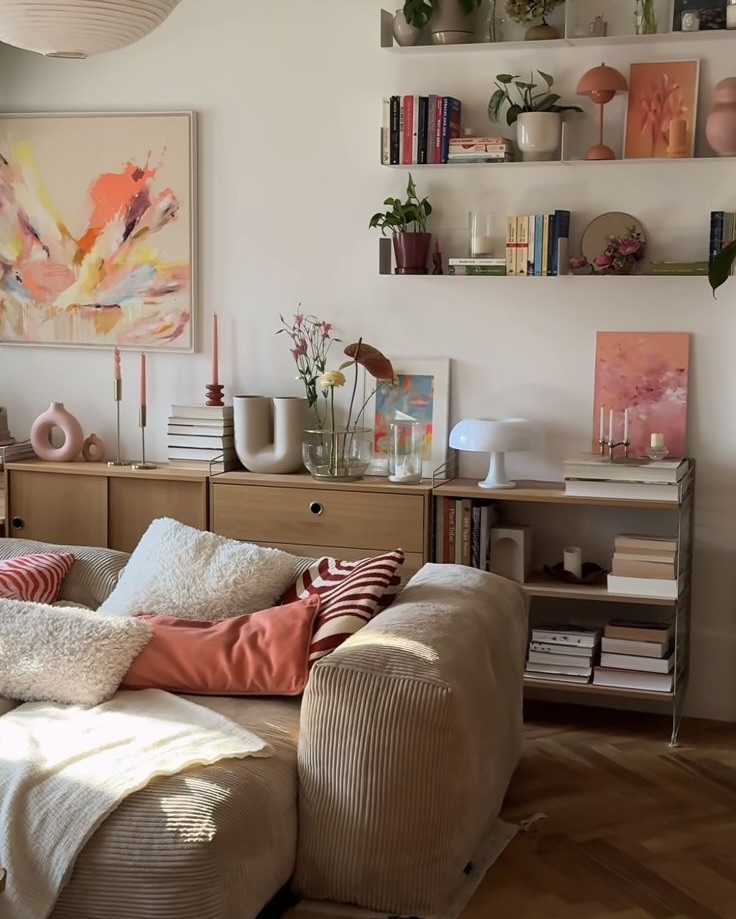 Salon chaleureux avec canapé en velours côtelé, coussins colorés, étagères de livres et décorations aux tons rose et orange.