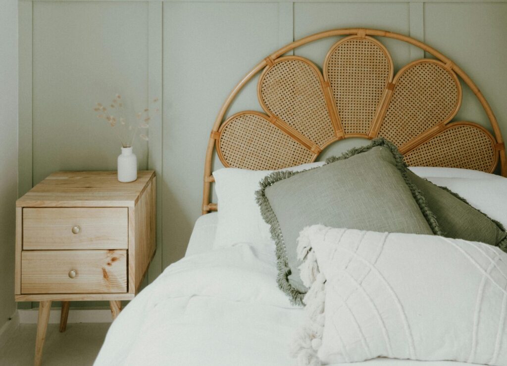 tête de lit en rotin avec lits/draps blancs et taies d'oreillers vertes et table de nuit en bois